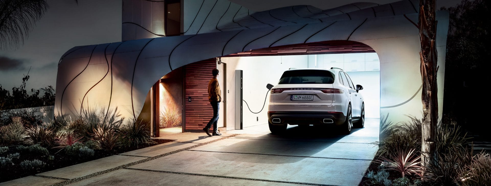 Porsche Cayenne sähköauton latauspisteessä modernin talon autotallissa.