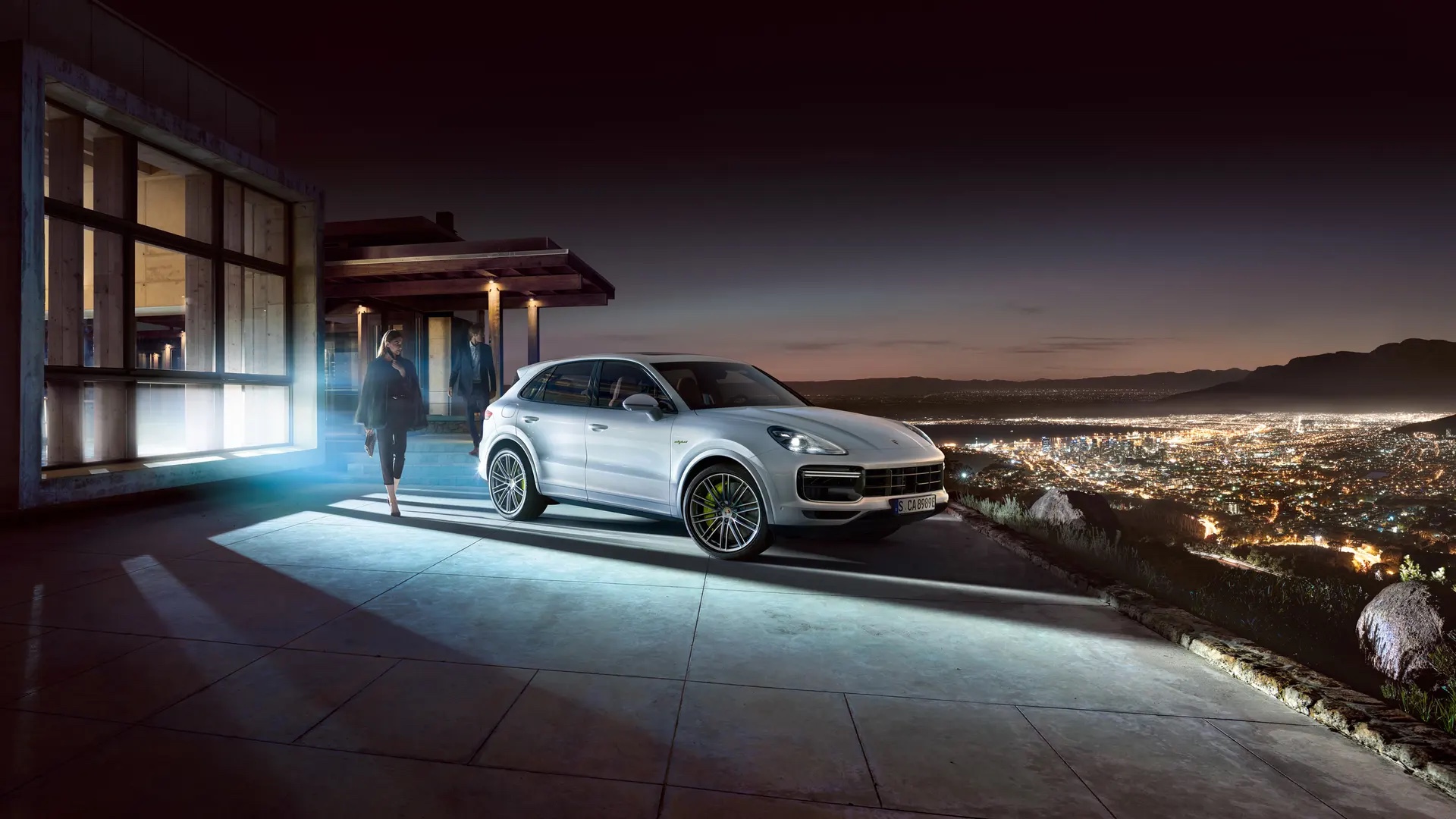 Porsche Cayenne vuoren päällä taustanaan valaistu kaupunki.