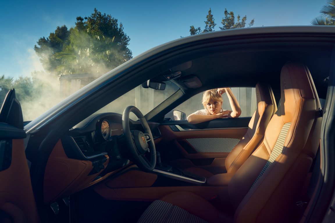 Nainen nojaamassa ikkunasta ja katsomassa Porsche 911:sta tyylikkäällä, sekä klassisella beigen värisellä sisustuksella.