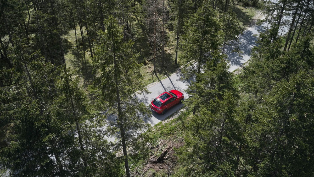 Punainen Porsche Cayenne ajamassa luonnossa.