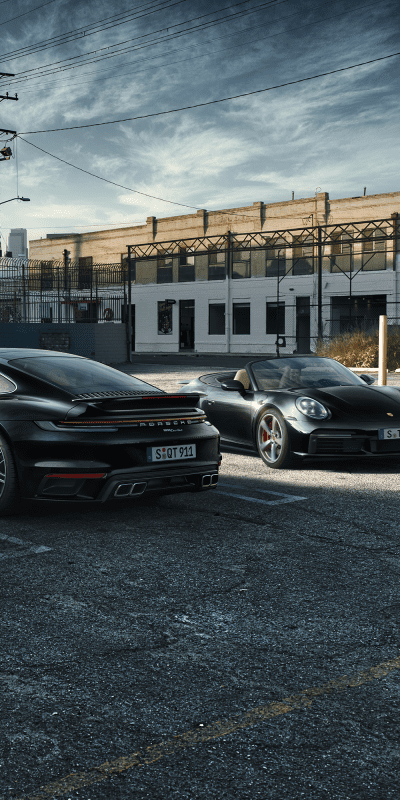 Kaksi mustaa Porsche 911 turboa parkkipaikalla.