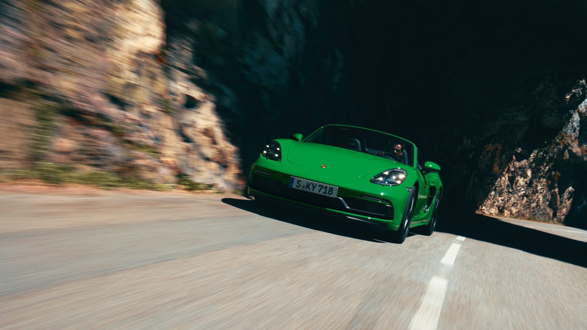 Vihreä Porsche 718 Boxster ajaa tiellä etuprofiili.